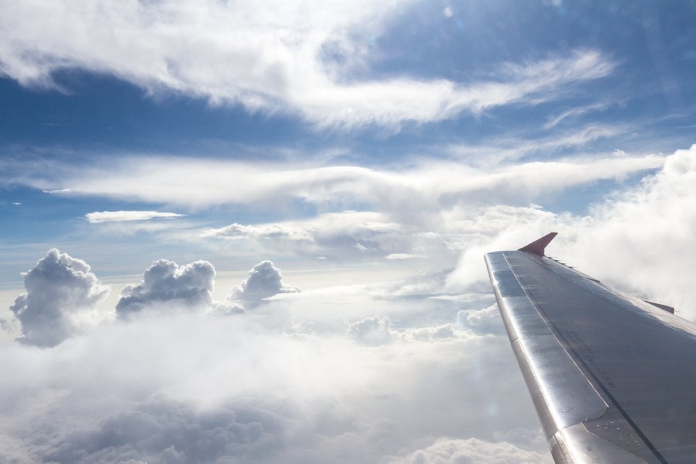 旅客機の窓から見た主翼と、青空に湧き上がる白い雲