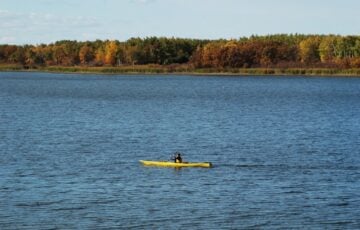 紅葉の森に囲まれた湖を黄色いカヤックで進む人
