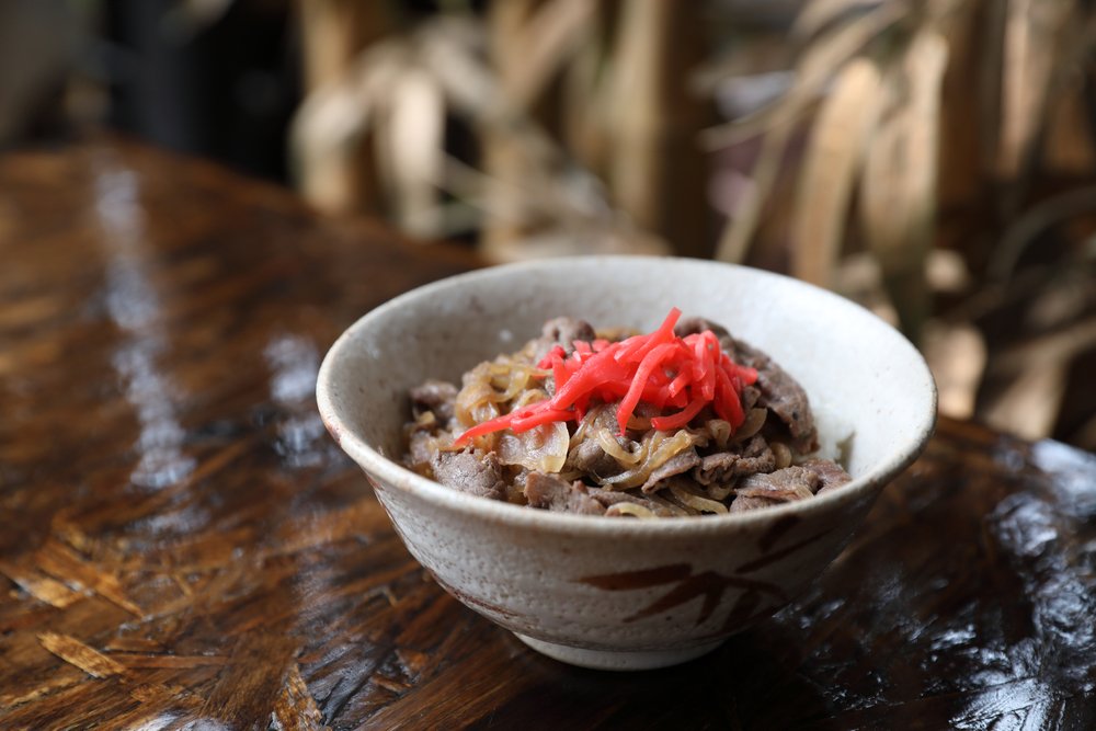木のテーブルに置かれた陶器の器の牛丼と紅しょうが