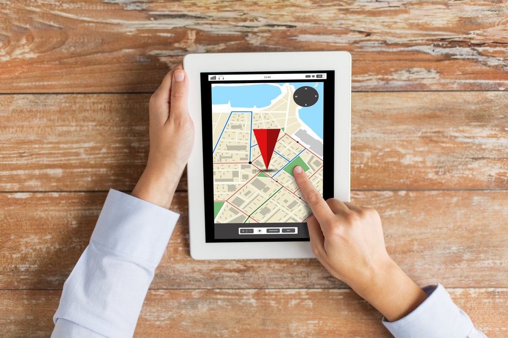 木のテーブルでタブレットの地図画面を指で操作する手元