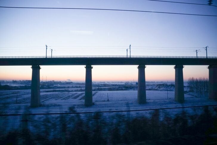 列車の窓から見た雪原と高架橋、夜明けの空